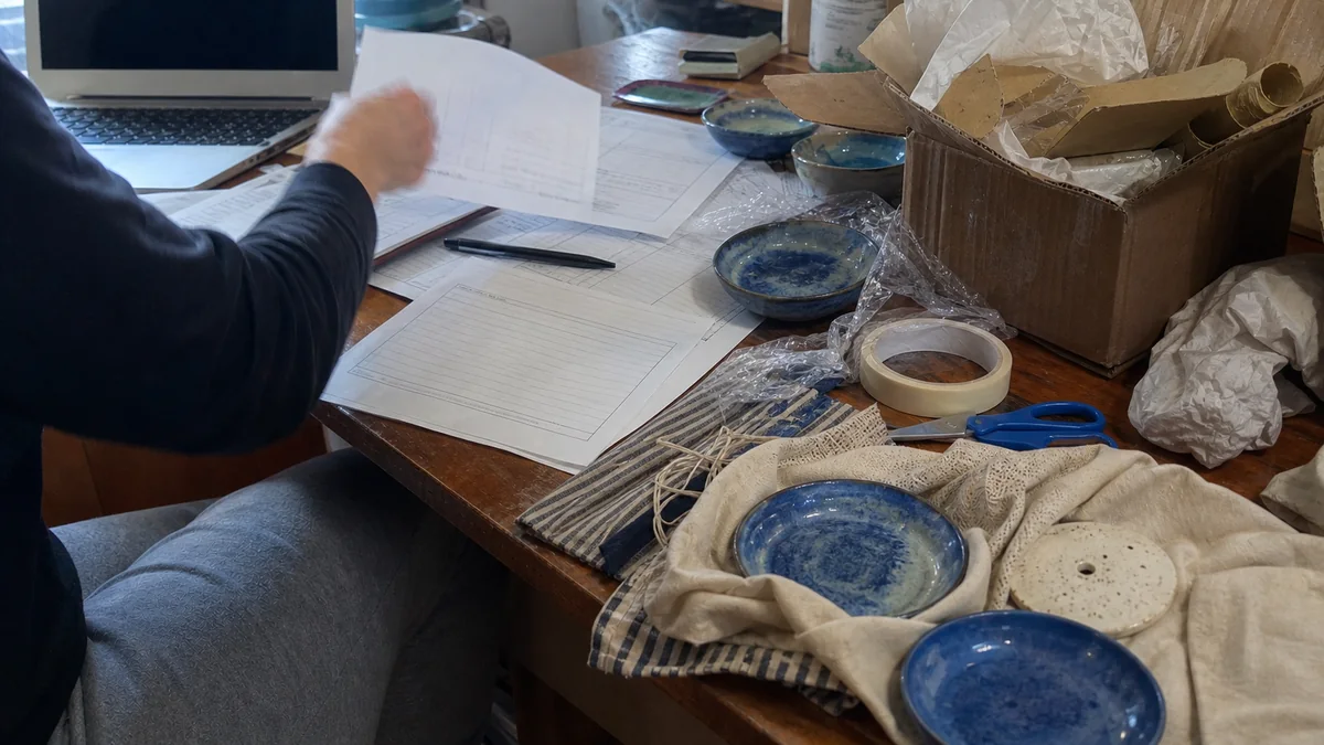 Ceramista revisando una solicitud junto a piezas y materiales de embalaje